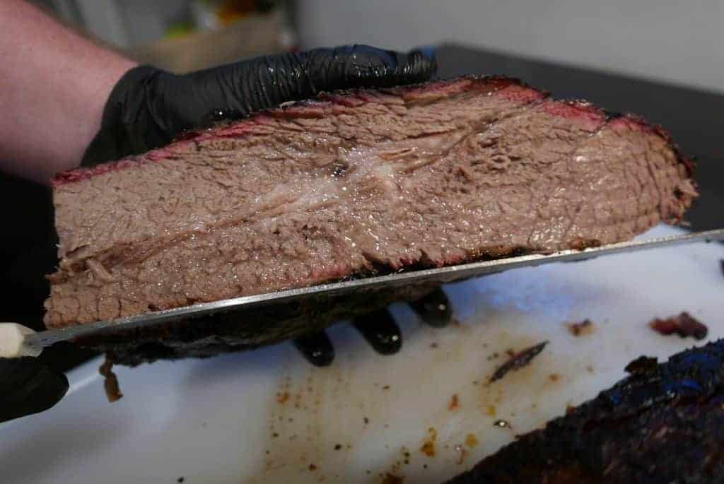 Man Holding A Sliced Smoked Brisket Over A White Cutting Board