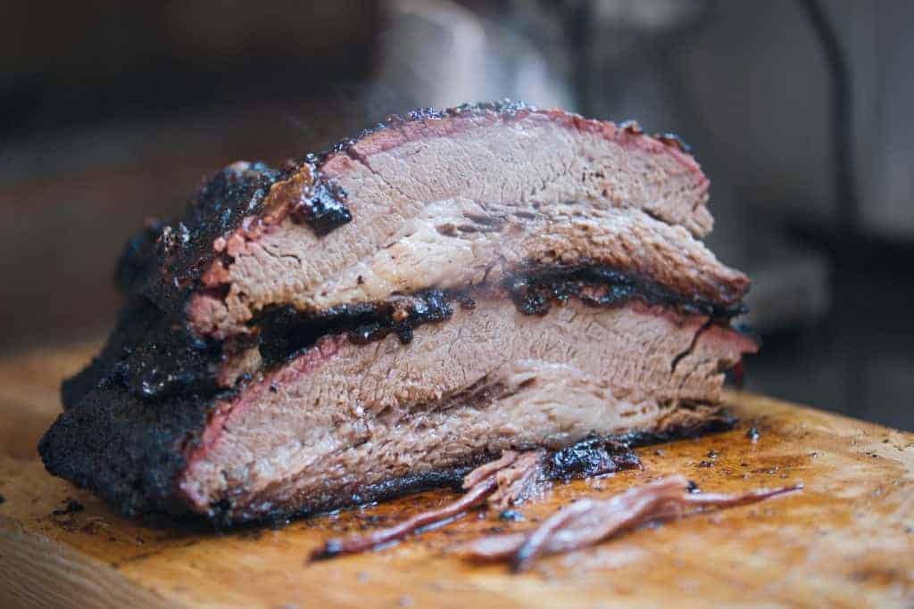 Two Large Pieces Of Smoked Brisket Meat On A Wooden Board